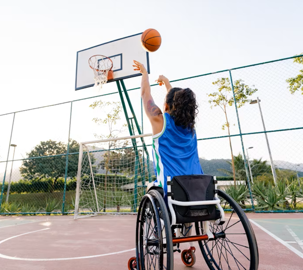 Personne en fauteuil roulant en train de lancer un ballon de basketball sur un terrain extérieur.